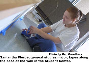 Samantha Pierce, general studies major, tapes along the base of the wall in the Student Center. 
