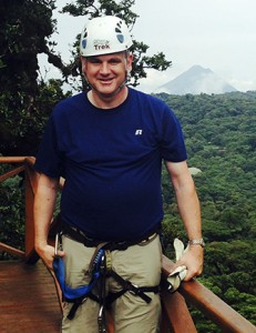 Mark Greger, associate professor of Spanish and faculty trip leader, prepares to zip line through a Costa Rican cloud forest with Arenal Volcano off in the distance. Contributed.