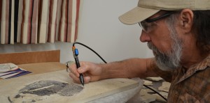 Billy Morris uses a tool to scrape away rock and expose the fossil underneath. The fossil Morris is preparing above was so well preserved that the fossil still has skin on it. Photo by Catie Sullivan