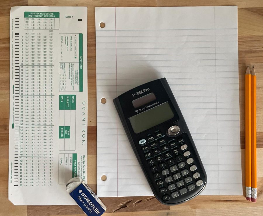 Scantron sheet, number two pencils, a calculator, and scrap lined paper laid out on a clear table to showcase what students need to take their in-person exams.