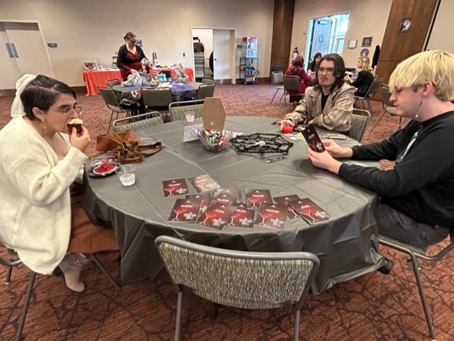 Students dressed up as vampires and are enjoying food before trying to figure out who the murderer is.